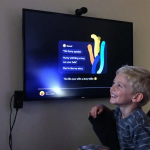 Мальчик улыбается, слушая забавную историю, которую рассказывает AI сказочник на умной колонке.
